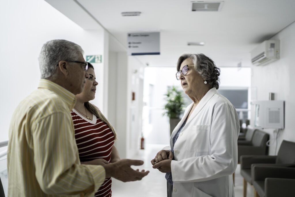 Female senior doctor talking about bad news and consoling sad family at hospital