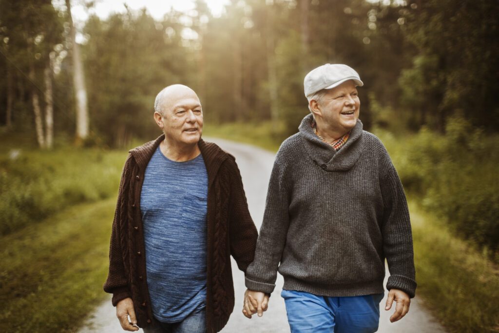 Happy gay couple looking away while walking on road amidst trees