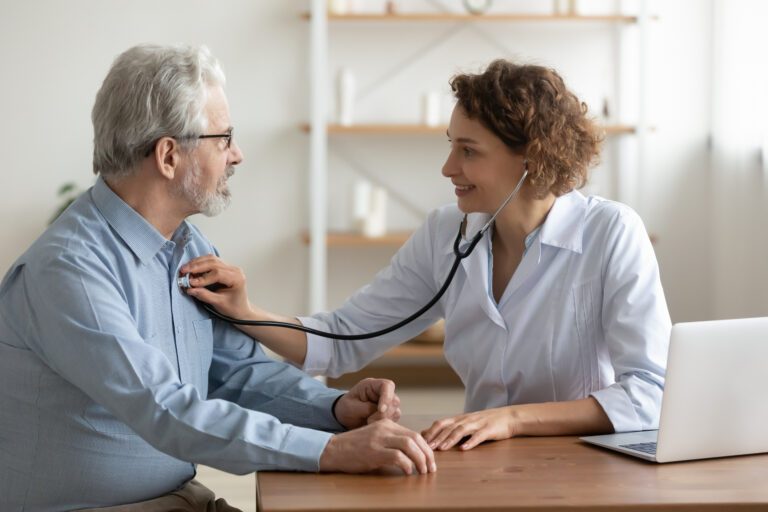 Female doctor listening senior male patient heart using stethoscope