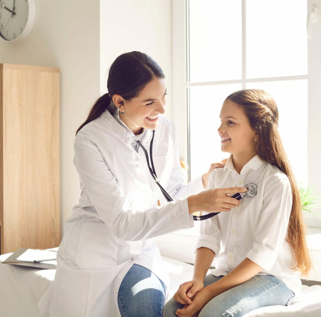 Happy child smiling while doctor is examining her lungs or heart during medical checkup